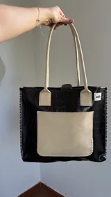 Bolso tote negro con textura símil cuero de cocodrilo, bolsillo externo color beige y asas marrones.