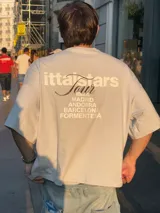 Remera rosa de corte recto con estampado en la espalda que incluye el texto "Itta Tours", "Tour", y nombres de ciudades como Ibiza, Madrid, Andorra, Barcelona y Formentera.