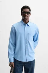 Camisa celeste de lyocell y algodón, corte relaxed fit, cuello solapa, manga larga con puños abotonados, bolsillo de parche en el pecho y cierre frontal con botones.