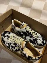 Zapatillas bajas con estampado animal print de vaca en blanco y negro, con cordones marrones y suela color caramelo.