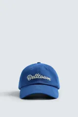 Gorra azul con visera confeccionada en tejido de algodón y parche frontal con texto bordado en blanco. Ajuste en la parte posterior.