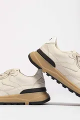 Zapatillas deportivas color beige con detalles en marrón y amarillo.