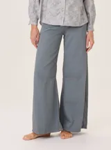 Pantalón ancho de color azul grisáceo, con corte holgado y pinzas debajo de la rodilla. Presenta pespuntes a contratono y bordado de monograma en el bolsillo delantero.