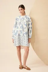 Vestido camisero corto de lino color blanco con estampado de estrellas de mar y algas en azul. Tiene cuello mao, mangas largas y cierre frontal con botones.