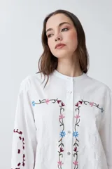 Camisa blanca con bordados florales en tonos rosa, azul y verde.