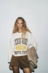 Sudadera blanca de algodón con cuello redondo y mangas largas. Estampado frontal con texto "Texas Rodeo 1995 United States" en color marrón.