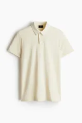 Remera polo de punto de algodón liviano color crema, de manga corta, corte ajustado y tapeta con botones.