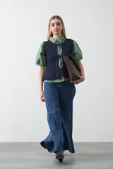 Chaleco tejido de punto color beige con trama texturada y diseño liviano. Presenta cuello a la base, silueta recta y cierre frontal mediante tres lazos delicados.