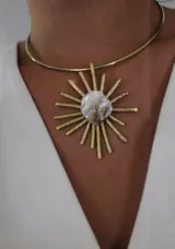 Gargantilla rígida dorada con dije central de nácar irregular rodeado de rayos dorados.