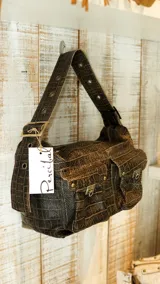 Bolso marrón con textura símil cuero de cocodrilo, con correa de hombro ajustable con hebilla y dos bolsillos frontales con cierre de hebilla metálica.