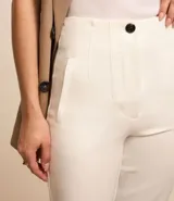 Pantalón zanahoria de sastrería color blanco, con cintura alta, trabillas y botón contrastante.