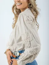 Camisa color crema de broderie, corte holgado, con cuello mao y mangas largas abullonadas con bordados florales.