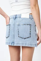 Minifalda de jean celeste con tiro bajo y detalle de tachas metálicas en los bolsillos.