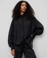 Camisa de calce amplio y tejido semitransparente, con cuello chimenea y mangas japonesas con puño. Presenta una botonadura frontal oculta y un acabado suave con brillo sutil y caída fluida.