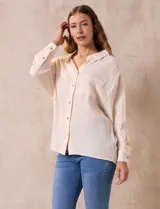 Camisa blanca de algodón con textura arrugada, cuello con solapa, abertura central con botones y bolsillo aplicado en el pecho. Mangas largas con largo regulable mediante presilla y botón.
