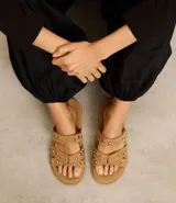 Sandalias planas color marrón claro con efecto gamuza y dos tiras con tachas doradas.