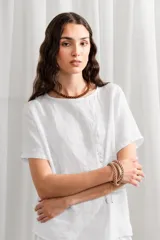 Blusa blanca de lino, corte holgado, con cuello redondo y cierre frontal con botones.
