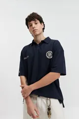 Remera polo azul marino con textura acanalada y corte oversize. Presenta cuello clásico con botones, mangas cortas y logo estampado en el pecho.