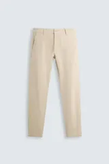 Pantalón chino color beige, corte skinny fit, confeccionado en tejido con mezcla de algodón y elasticidad. Cuenta con bolsillos frontales y traseros. Cierre frontal con cremallera y botón.