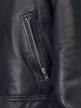 Chaqueta de cuero negra con cuello clásico, cierre frontal con cremallera, mangas largas con puños abotonados y bolsillos laterales con cremallera.