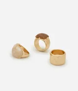 Set de tres anillos con diferentes diseños: uno dorado con textura, uno marrón con forma cuadrada y uno blanco marmolado.