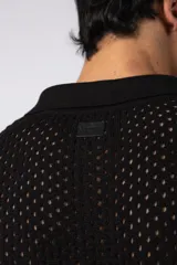 Camisa negra tejida de manga corta, con calado aireado, cuello tipo bowling y botones al tono. Diseño de corte relajado.