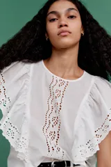 Blusa blanca de algodón con secciones en broderie. Modelo con mangas cortas de volados y cuello redondo con abertura de cerradura y botón oculto en la nuca.