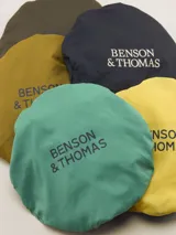 Gorro tipo bucket color mostaza con cinta decorativa a rayas horizontales en tonos bordó, amarillo y azul marino.