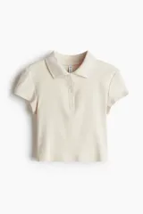 Remera polo color crema de punto acanalado, con cuello clásico, tapeta de botones y mangas cortas. Corte entallado.