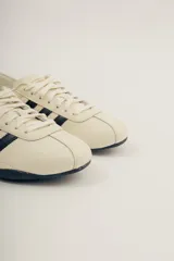 Championes Adidas Tokyo color crema con detalles en negro, con las tres tiras características de la marca en los laterales.