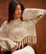 Sweater corto color crema, tejido a crochet con diseño calado y mangas acampanadas. Presenta flecos en el ruedo.