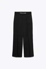 Pantalón negro de tiro medio con cinturón a tono con hebilla metálica, bolsillos delanteros y falsos bolsillos traseros.