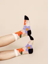 Medias de caña media transparentes con puño blanco con volados y estampado de flores rojas, amarillas y azules. Puntera y talón negros.