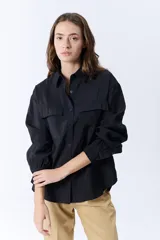 Camisa negra de manga larga con cuello clásico, cierre frontal con botones y dos bolsillos con solapa en el pecho.
