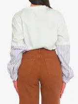 Remera blanca de algodón de corte amplio, con cuello redondo y mangas cortas con puños camiseros a rayas celestes y blancas.