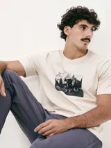 Camiseta blanca de algodón con cuello redondo y mangas cortas. Estampa rectangular con borde negro que contiene la frase "NATURAL ATMOSPHERE" en letras mayúsculas y una imagen de montañas y mar.