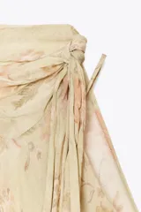 Vestido corto con estampado floral en tonos beige y rosa, escote pico y tirantes finos. Detalle de capa asimétrica con cuello subido y lazada. Forro interior combinado a contraste y bajo acabado con volantes.