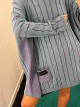 Sweater negro de punto con diseño de trenzas, corte holgado, mangas largas y bolsillos frontales. Tejido artesanalmente en Uruguay, con puños altos ajustados.