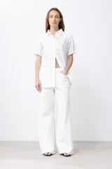 Camisa verde con cuello clásico, manga corta y cierre frontal con botones. Presenta diseño patchwork con detalles de broderie y calados.