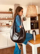 Bolso de hombro grande de cuero negro, con correa ancha y bolsillo interno con cierre.