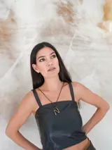 Gargantilla marrón de cuero con dije de bronce en forma de letra M.