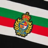 Camiseta negra de punto con cuello polo y mangas cortas. Presenta una franja horizontal con los colores de la bandera italiana y un escudo bordado en el pecho. Tiene el logo de Corteiz bordado en el lado izquierdo y las letras RTW bordadas en el centro.