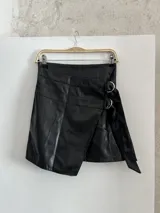 Minifalda negra de ecocuero con diseño cruzado y detalle de argollas metálicas.