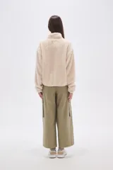 Buzo de polar tipo sherpa en color crudo, con cuello alto y cierre frontal parcial. Presenta un bolsillo de parche con cierre en el pecho y mangas largas de calce holgado.