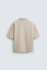 Polo color beige de corte relaxed fit, confeccionado en tejido interlock de algodón con elasticidad. Tiene cuello solapa con cierre frontal de cremallera y manga corta.