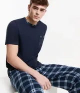 Conjunto de pijama largo para hombre, compuesto por una remera de manga corta azul marino con bolsillo en el pecho y un pantalón largo con cintura elástica y estampado de cuadros azules y blancos.
