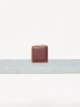 Billetera pequeña de cuero vacuno color bordó con cierre metálico y aplique de hongo. Interior con divisiones para tarjetas y forrería de tejido jacquard.