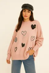 Sweater rosa de lanilla con cuello redondo y mangas largas. Presenta apliques de corazones en diferentes estilos: bordados, con brillos y con textura.