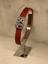 Cinturón de cuero color marrón con hebilla metálica plateada con diseño de serpientes entrelazadas.