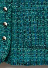 Chaqueta de tweed color verde azulado con cuello redondo, cierre frontal con botones efecto joya, dos bolsillos de parche delanteros, terminaciones deshilachadas y forro interior.